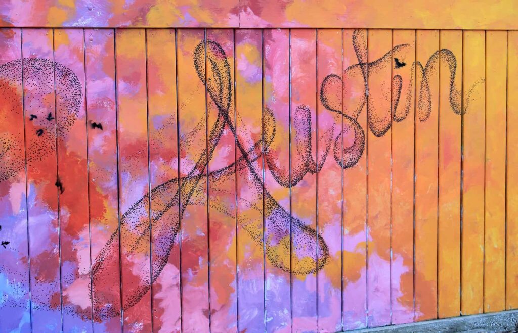 A multicolored painted fence with the word Austin painted in dots to represent flying bats